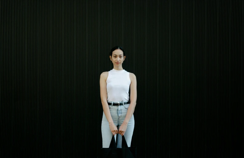 a woman standing in front of a black wall, white tank top, kiko mizuhara, taken with sony alpha 9, low quality photo