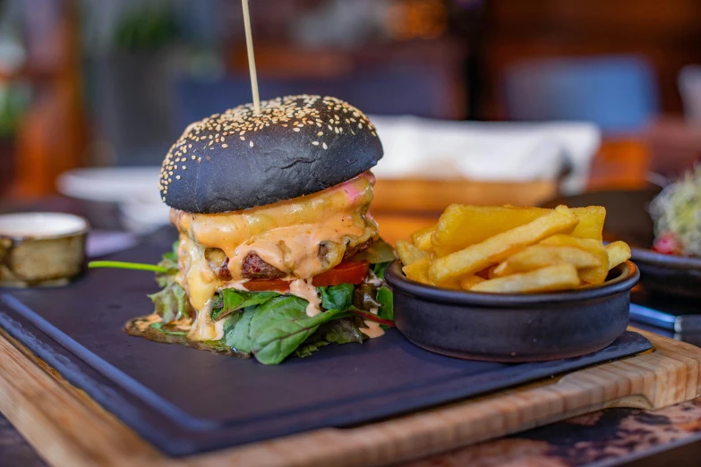 a burger sitting on top of a black plate next to a bowl of fries, unsplash, toki doki, daily specials, 🦩🪐🐞👩🏻🦳, woodfired