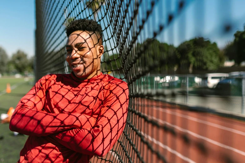 a man in a red shirt leaning against a fence, pexels contest winner, happening, wearing a track suit, photo of a black woman, wearing fitness gear, very excited