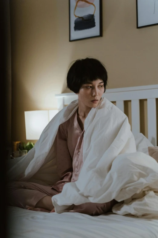 a woman sitting on a bed under a blanket, with short hair, female actress from korea, worried, ( ( theatrical ) )