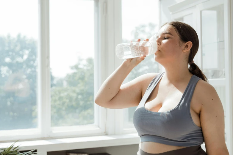 a woman standing in front of a window drinking a glass of water, peter griffin body type, wearing crop top, sweat and labour, profile image