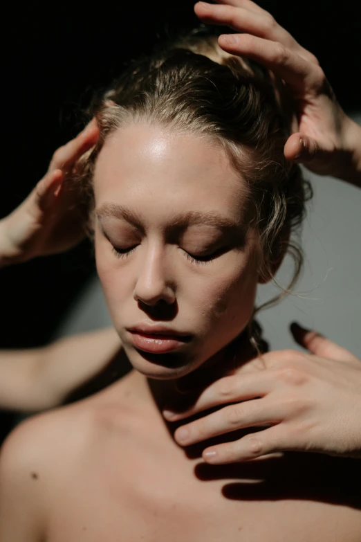 a woman standing in front of a mirror with her hands on her head, inspired by Elsa Bleda, renaissance, with textured hair and skin, inside her temple, in front of a black background, acupuncture treatment