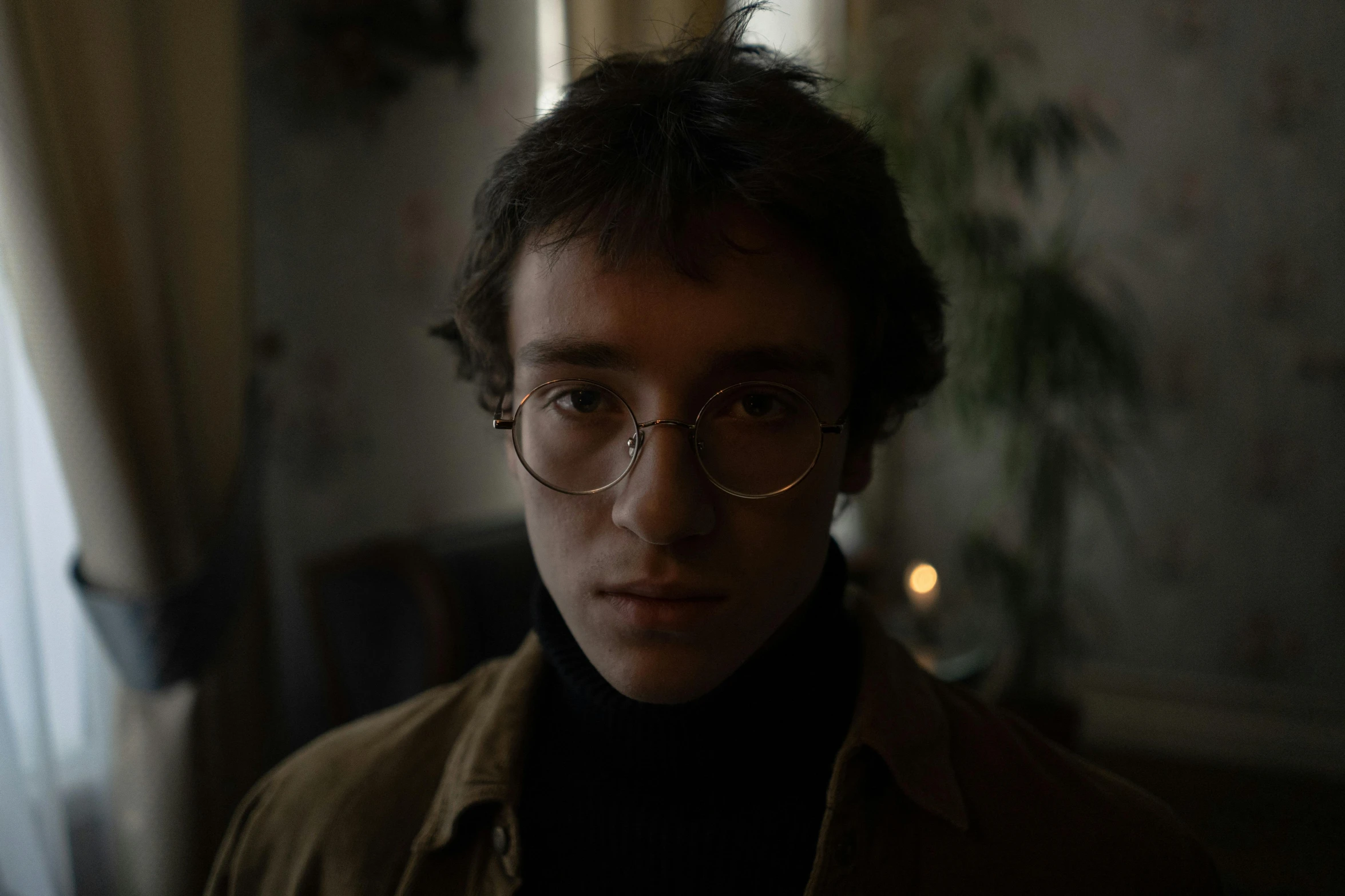 a close up of a person wearing glasses, a character portrait, by Attila Meszlenyi, pexels contest winner, wearing a turtleneck and jacket, young male, standing in a dimly lit room, low quality footage