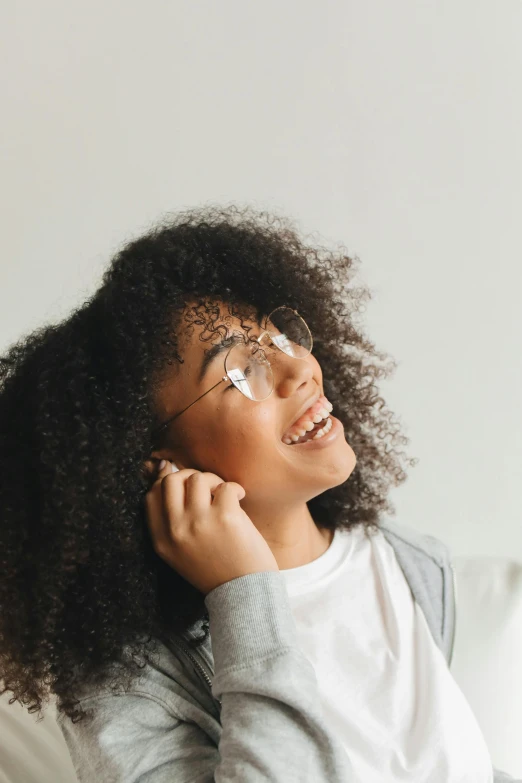 a woman sitting on a couch talking on a cell phone, trending on pexels, afrofuturism, square rimmed glasses, side portrait of cute girl, with curls, pictured from the shoulders up