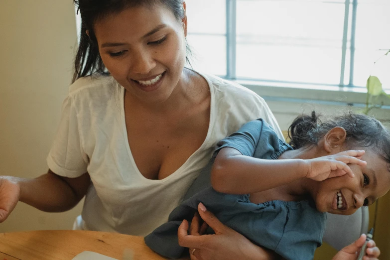 a woman holding a child in front of a laptop, pexels contest winner, manuka, sitting on a table, health supporter, holding an epée