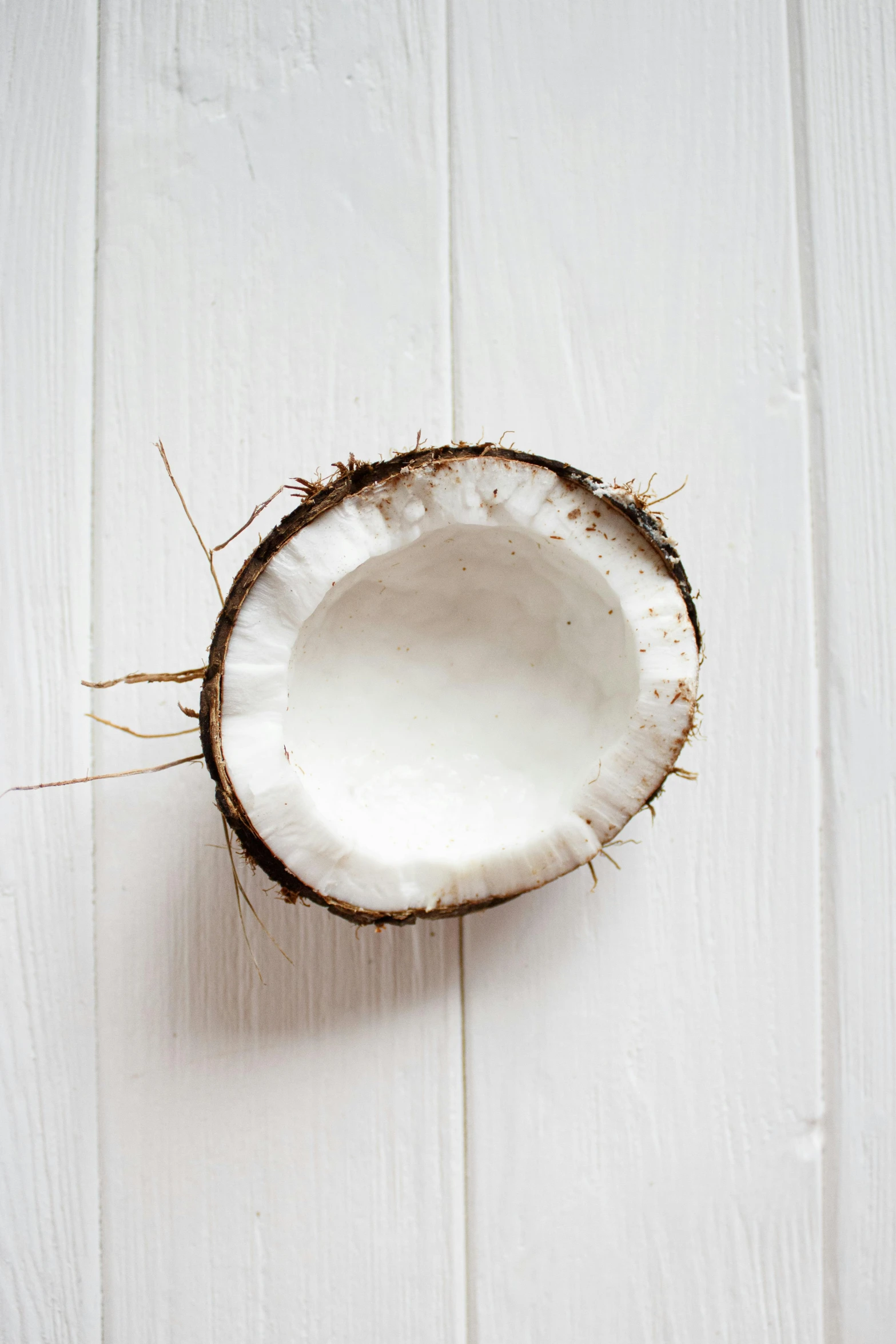 a half of a coconut sitting on top of a wooden table, a picture, by Felicity Charlton, unsplash, white wall, made of glazed, natural soft rim light, on white background