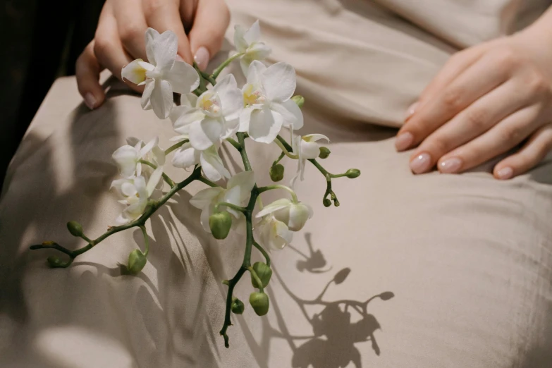 a close up of a person holding a flower, wearing white silk robe, laying down, orchids, neutral colours