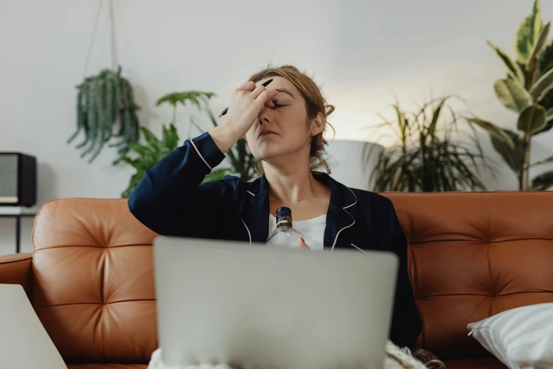 a woman sitting on a couch with her head in her hands, trending on pexels, sitting at a computer, wet eye in forehead, drinking cough syrup, people at work