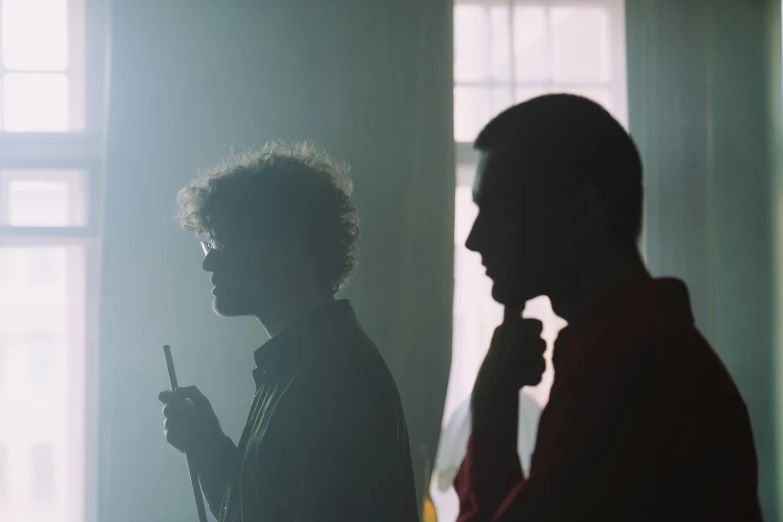 a man and a woman standing in front of a window, inspired by Nan Goldin, pexels, serial art, two young men, smoking, back lighting, calmly conversing 8k