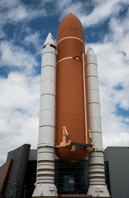 a large space shuttle sitting on top of a building, orange and white, rocket, back facing the camera, a bald