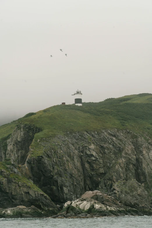 a small island with a lighthouse on top of it, unsplash, under a gray foggy sky, helicopter, hillside, 8 k film still