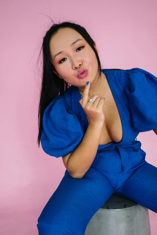 a woman sitting on top of a cement stool, inspired by Jean-Auguste-Dominique Ingres, featured on reddit, blue outfit, young asian woman, thick lips, wearing human air force jumpsuit