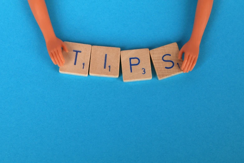 a close up of a person holding wooden blocks with the word tips written on them, a cartoon, trending on pixabay, blue, aardman animation, decorations, splash image