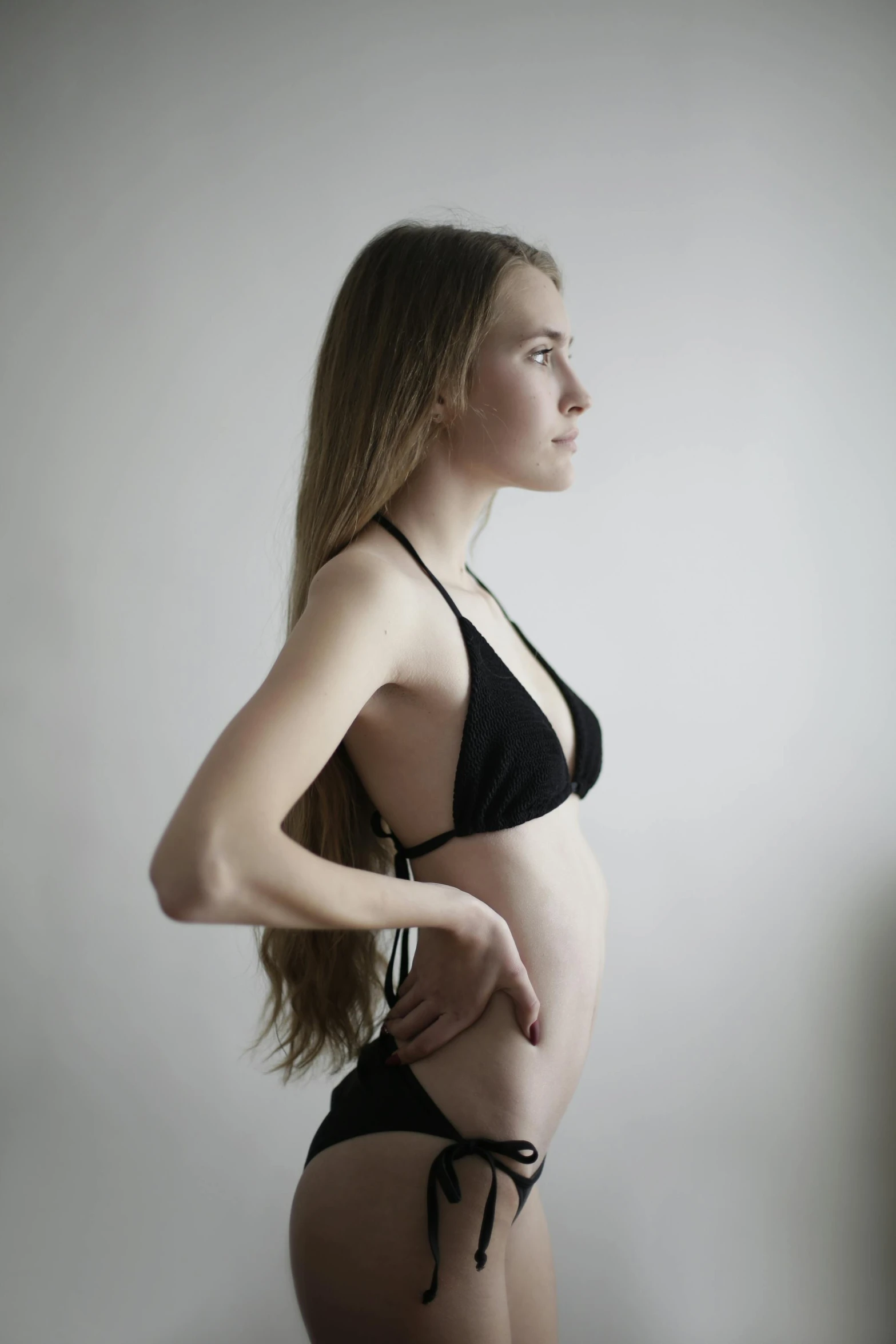 a woman in a black bikini posing for a picture, an album cover, inspired by Louisa Matthíasdóttir, unsplash, renaissance, sideview, young and slender, pregnant, wearing a crop top