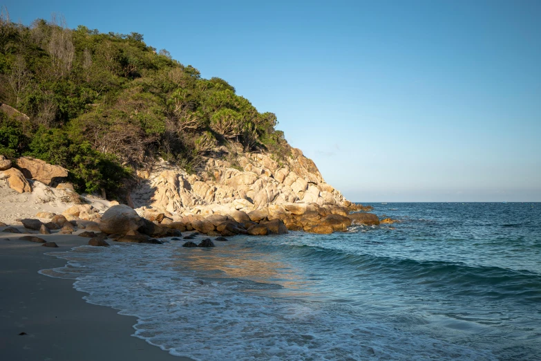 a large body of water sitting on top of a sandy beach, by Elizabeth Durack, unsplash, in the distance is a rocky hill, beach and tropical vegetation, dappled in evening light, conde nast traveler photo