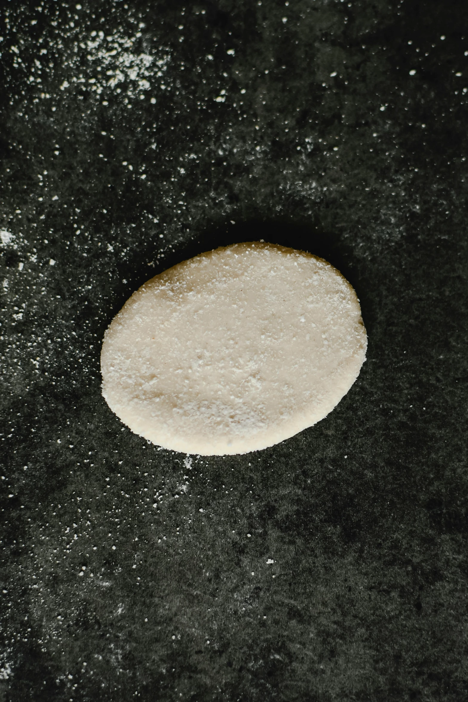 a piece of bread sitting on top of a black surface, flat pancake head, covered in white flour, 2 0 mm, round narrow chin