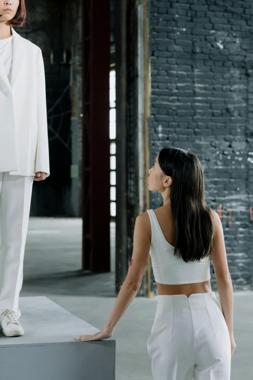 a woman standing next to a man in a white suit, inspired by Vanessa Beecroft, renaissance, in a warehouse, madison beer, foreground background, [ theatrical ]