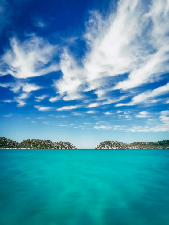 a large body of water with a small island in the background, teal studio backdrop, epic skies, abel tasman, ibiza