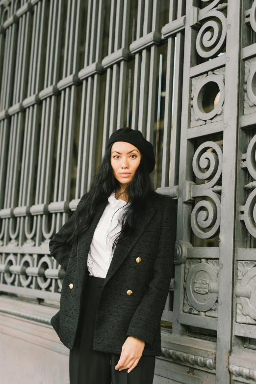 a woman standing in front of a metal gate, black beret, wearing a blazer, with long black hair, yulia nevskaya