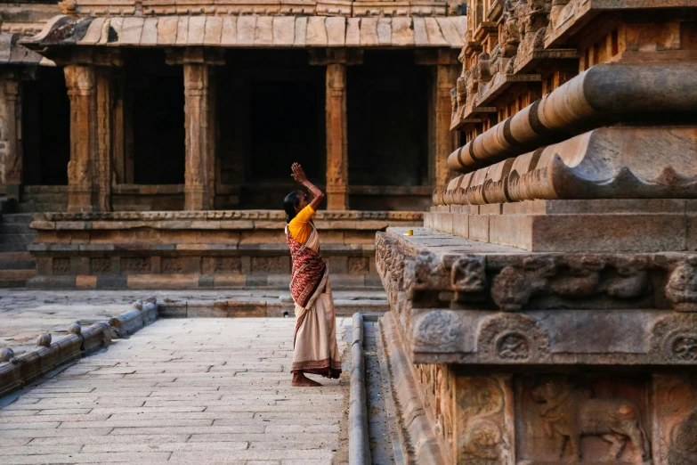 a woman standing in front of a stone structure, pexels contest winner, hindu ornaments, trampling an ancient city, ancient library, facing away