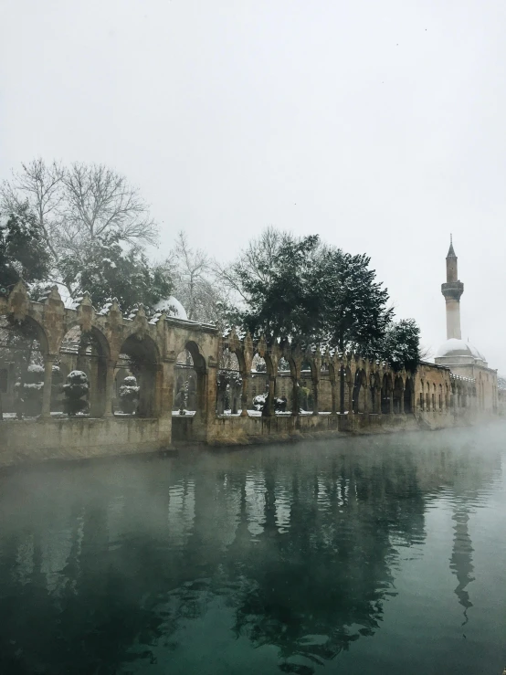 a body of water with a clock tower in the background, by Abdullah Gërguri, pexels contest winner, hurufiyya, winter mist around her, cypresses, low quality photo, today\'s featured photograph 4k