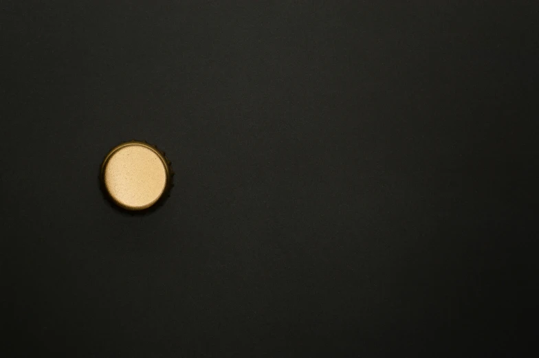 a close up of a button on a black surface, by Ottó Baditz, unsplash, gold eyeshadow, minimalissimo, offering the viewer a pill, ignant