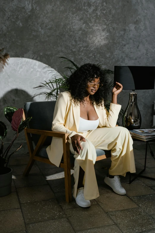 a woman sitting in a chair in a room, inspired by Esaias Boursse, trending on pexels, tan suit, lizzo, lemonade, black young woman