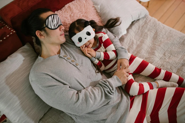 a woman and a child laying on a bed, inspired by The Family Circus, pexels contest winner, wearing bandit mask, dad energy, stripe over eye, manuka