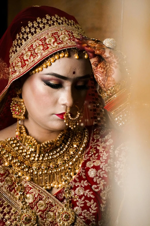 a woman dressed in a red and gold outfit, by Sudip Roy, pexels contest winner, his head covered in jewels, bride, square, looking left