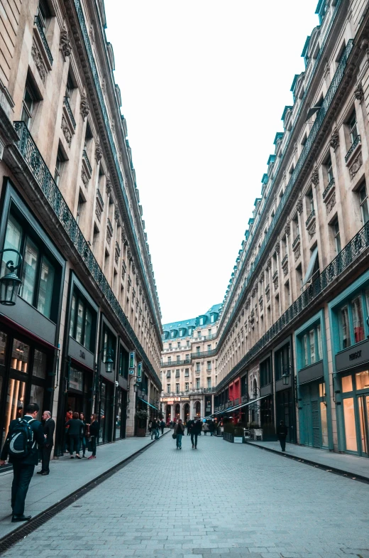 a group of people walking down a street next to tall buildings, neoclassicism, parisian buildings, stores, maze of streets, empty streetscapes