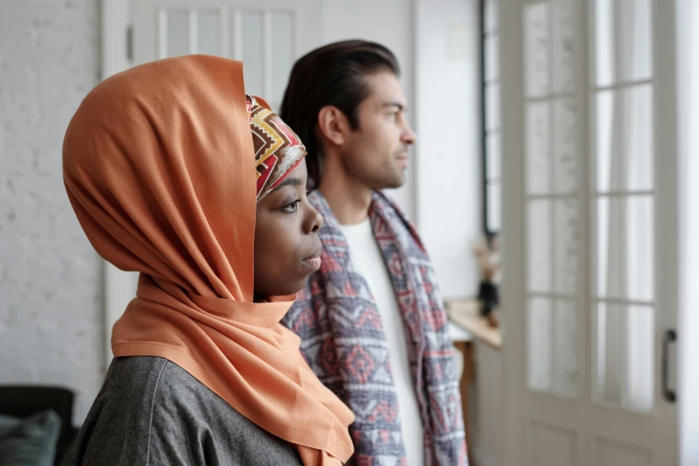 a man and a woman standing next to each other, pexels contest winner, hurufiyya, wearing a head scarf, at home, looking off to the side, profile image