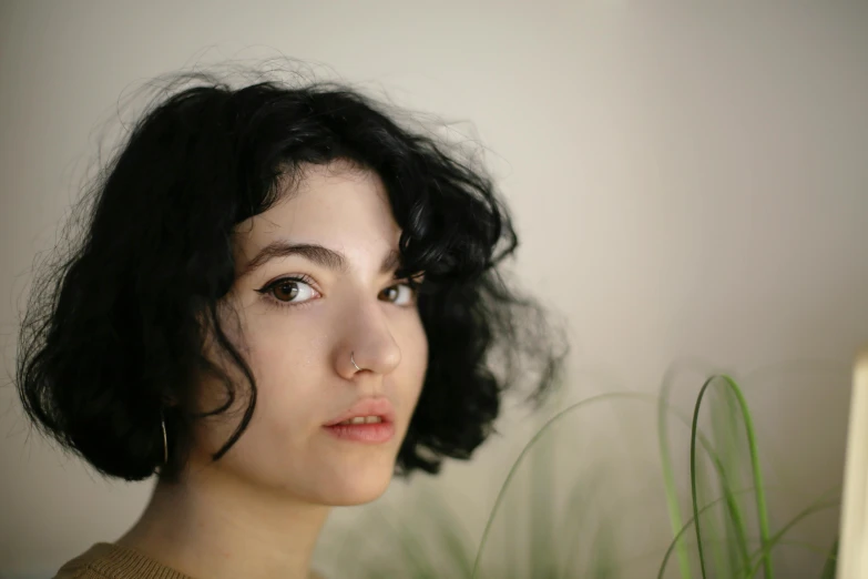 a woman sitting in front of a laptop computer, an album cover, trending on pexels, photorealism, bushy eyebrows, short black curly hair, portrait mode photo, with soft bushes