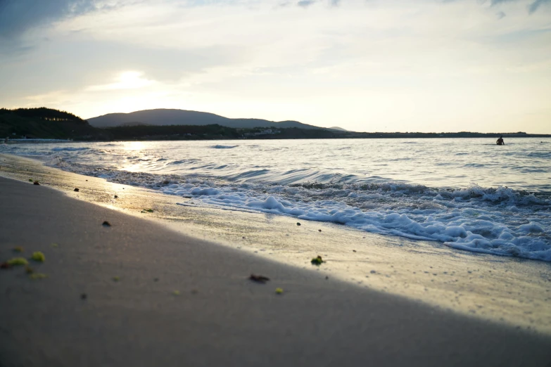 a person riding a surfboard on top of a sandy beach, which shows a beach at sunset, croatian coastline, distant photo, conor walton