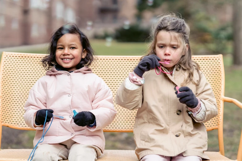 a couple of young girls sitting on top of a wooden bench, pexels contest winner, american barbizon school, fingerless gloves, julia hetta, tiny sticks, warm friendly expression