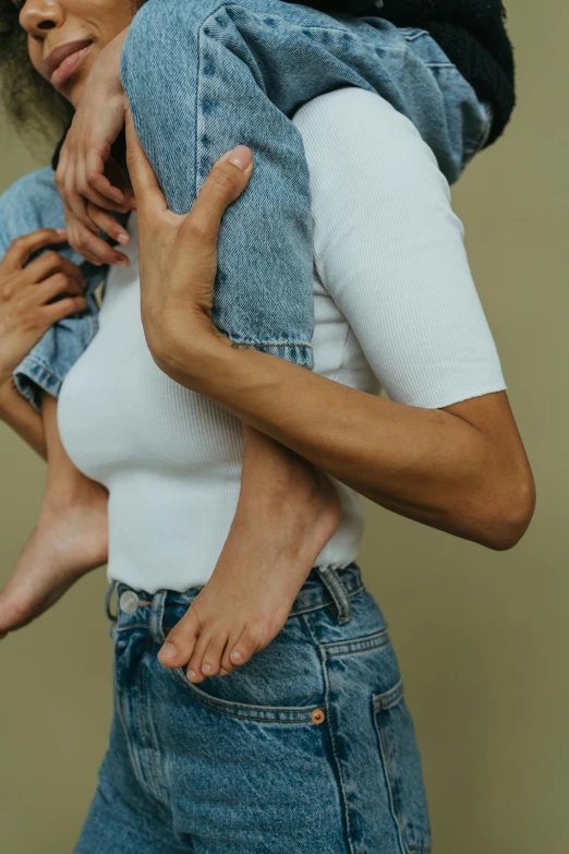 a woman holding a baby in her arms, an album cover, by Nina Hamnett, trending on pexels, aestheticism, jeans, human bodies intertwined, palm body, solid background