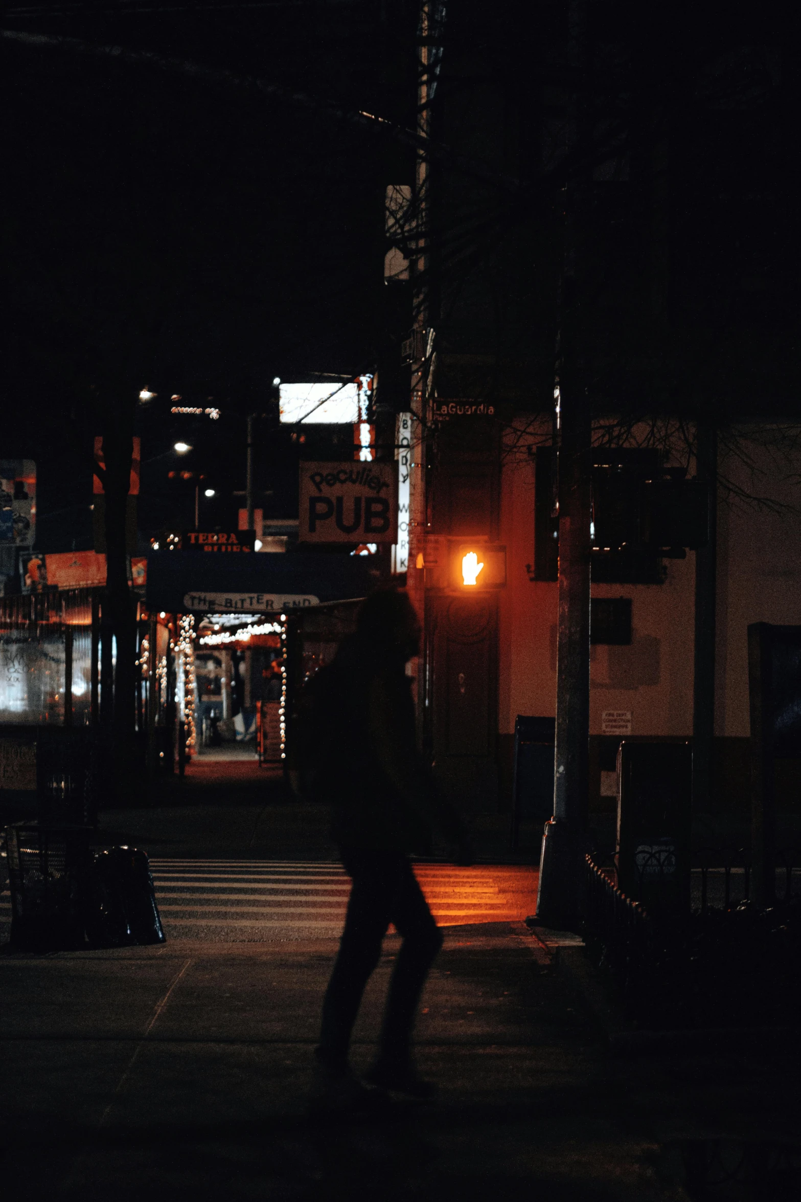 a person walking across a street at night, japanese town, light and dark, orange lights, with a black background