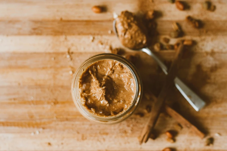 a jar of peanut butter sitting on top of a wooden table, by Emma Andijewska, pexels, cinnamon skin color, flatlay, spoon, background image