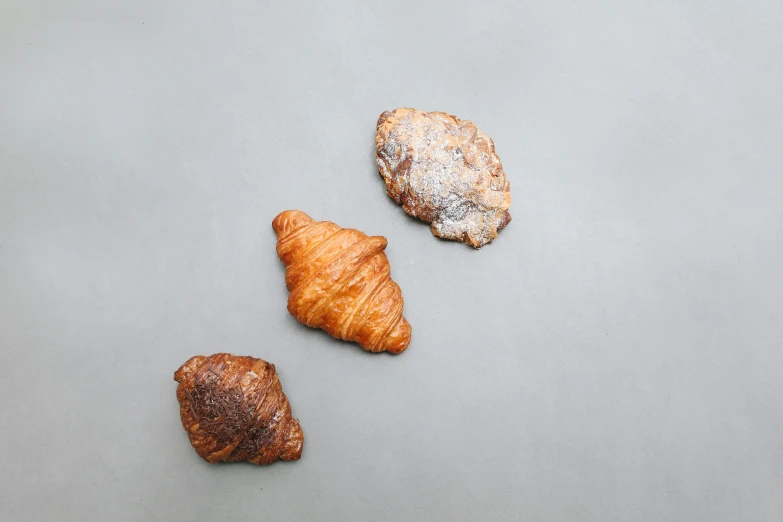 a couple of croissants sitting on top of a table, the three moiras, on a gray background, top - down photograph, chicago