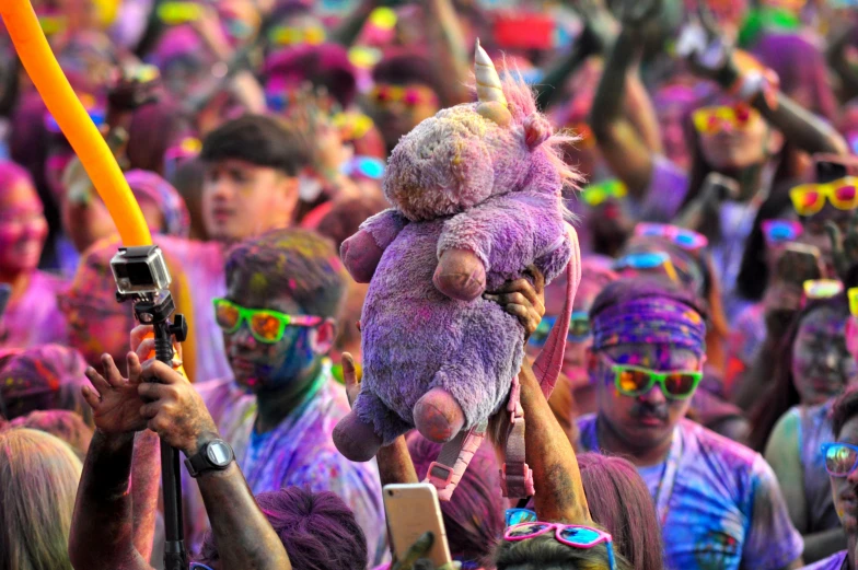 a person holding a stuffed animal in front of a crowd of people, pexels contest winner, color field, vibrant powder paints, the spirit of the bull run, seapunk, purple neon colours