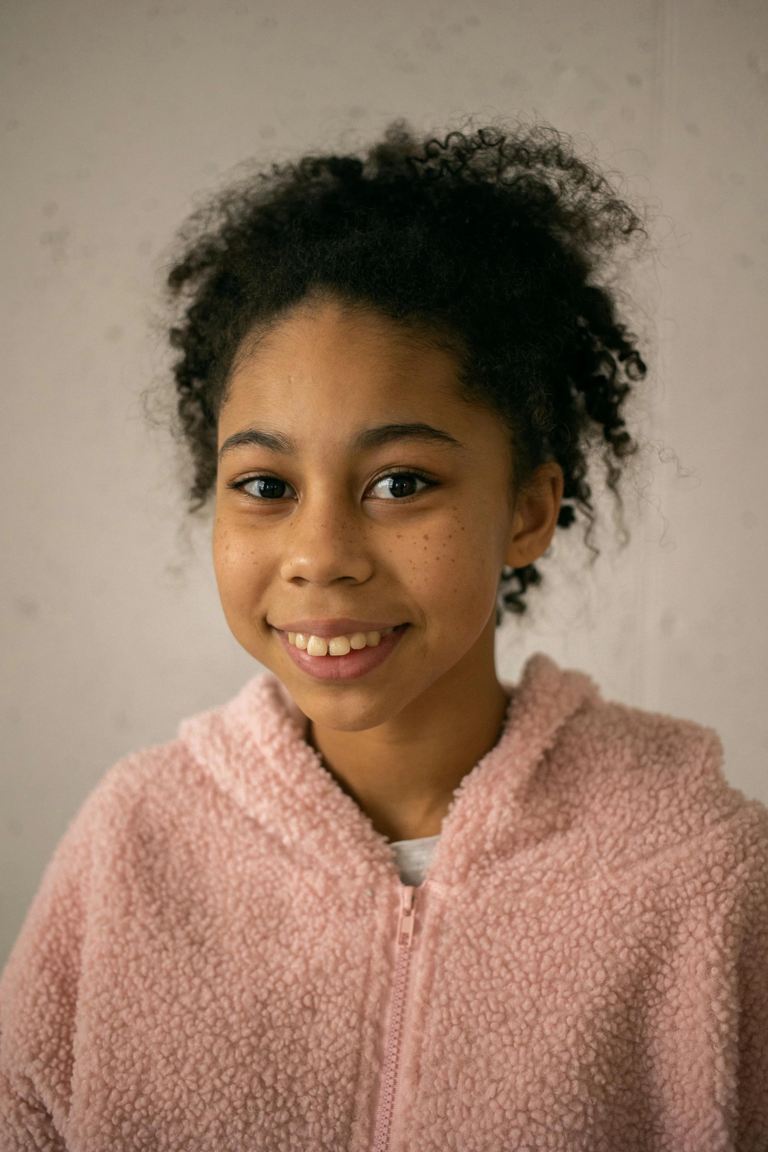 a young girl in a pink jacket smiles at the camera, by Daniel Seghers, light-brown skin, promo image, indoor picture, child hybrid