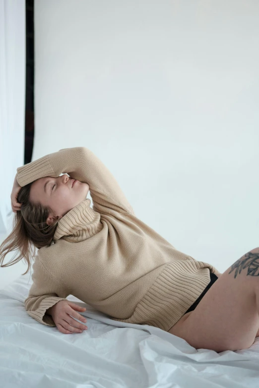 a woman laying on top of a white bed, inspired by Elsa Bleda, trending on unsplash, visual art, wearing turtleneck, beige, tattooed, full body model