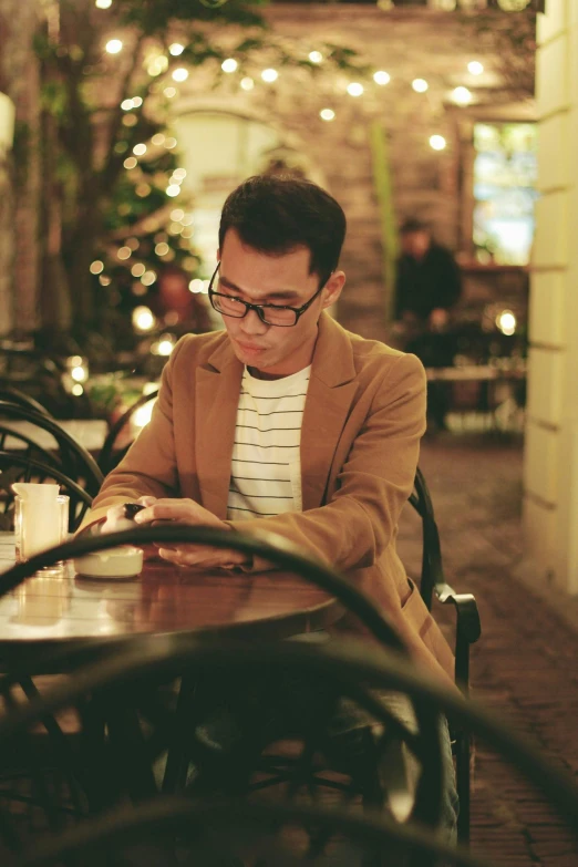 a man sitting at a table using a cell phone, by Robbie Trevino, happening, in square-rimmed glasses, cosy, darren quach, stylish