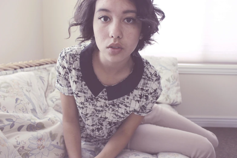 a woman sitting on top of a bed next to a window, an album cover, inspired by Yuko Tatsushima, unsplash, rococo, cute pout, aubrey plaza, messy short hair, ((portrait))