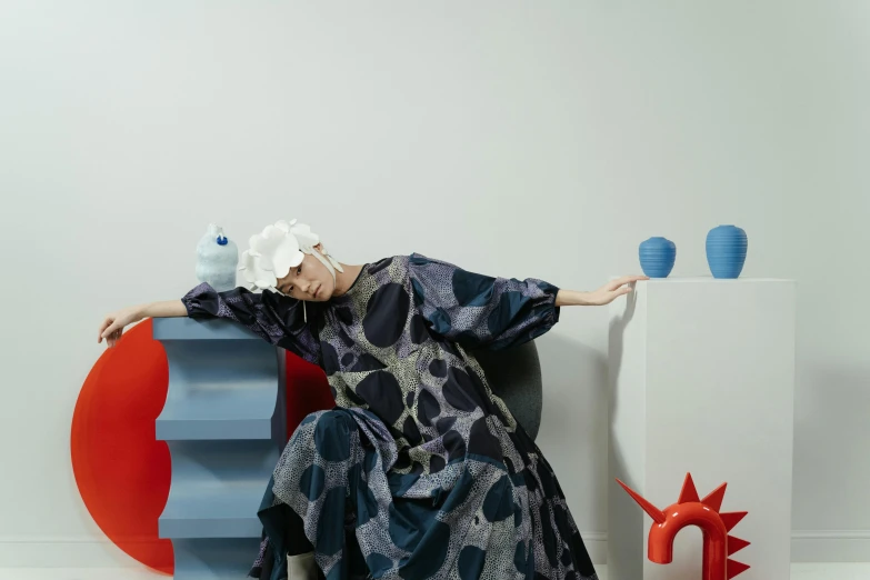 a woman sitting on a chair in a room, a surrealist sculpture, inspired by Gao Cen, unsplash, maximalism, wearing blue robe, an oversized beret, lying on an abstract, patterned clothing