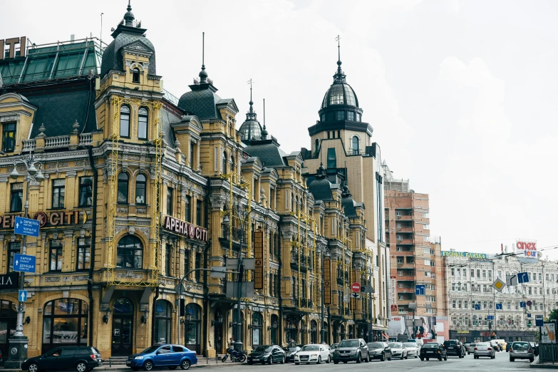 a group of cars driving down a street next to tall buildings, by Serhii Vasylkivsky, pexels contest winner, art nouveau, rostov city, victorian buildings, where a large, tula