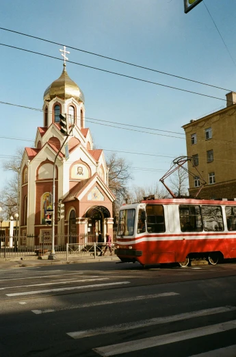 a red and white bus driving down a street next to a church, inspired by Vladimir Tatlin, pexels contest winner, socialist realism, shades of aerochrome gold, square, street tram, 000 — википедия