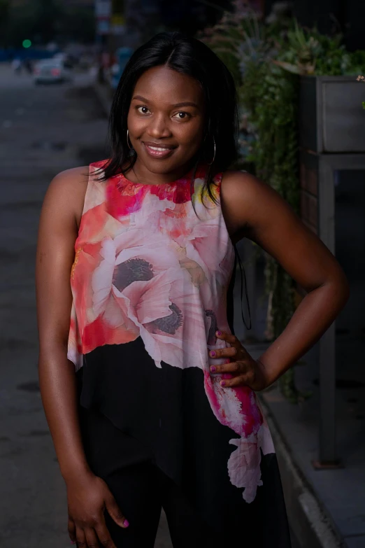 a woman standing on a sidewalk with her hands on her hips, by Chinwe Chukwuogo-Roy, acting headshot, floral painted backdrop, she is wearing a black tank top, ( ( dark skin ) )