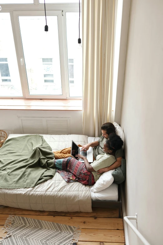 a woman laying on top of a bed next to a window, happening, two buddies sitting in a room, connectivity, apartment, couple on bed