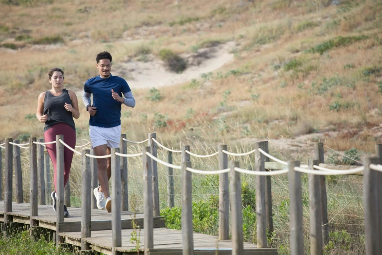 a couple of people that are running on a bridge, dunes in the background, manuka, avatar image, outdoor photo