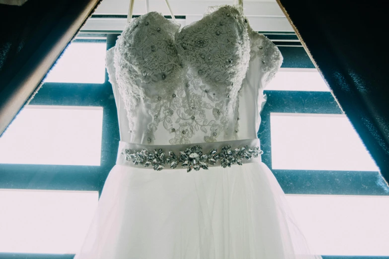 a wedding dress hanging in front of a window, by Joe Bowler, pexels contest winner, ornate with diamonds, white and silver, full front view, snapchat photo